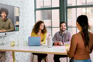 A team having a small hybrid meeting with o conference, in a small workspacesome people joining via vide